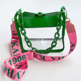 Alpha Kappa Alpha clear plastic handbag with a bright green faux-leather top flap, green chain detail, and a wide pink shoulder strap printed with green letters and numbers.